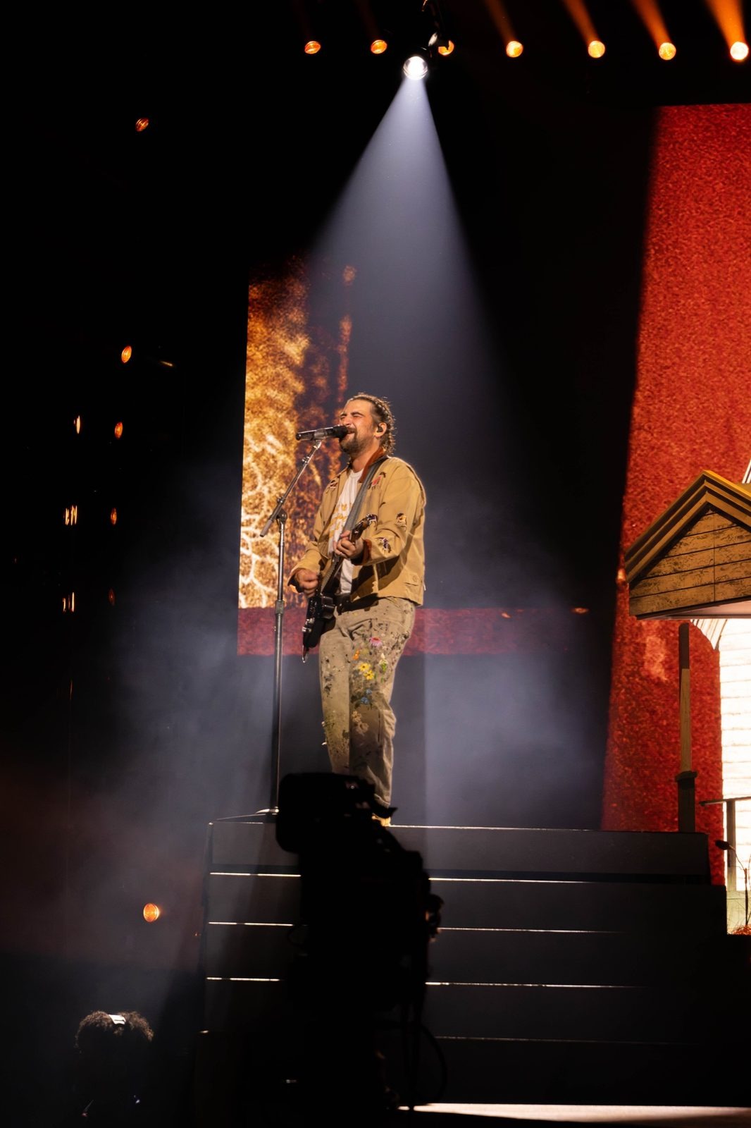 Performer on a raised platform under a white spotlight beam