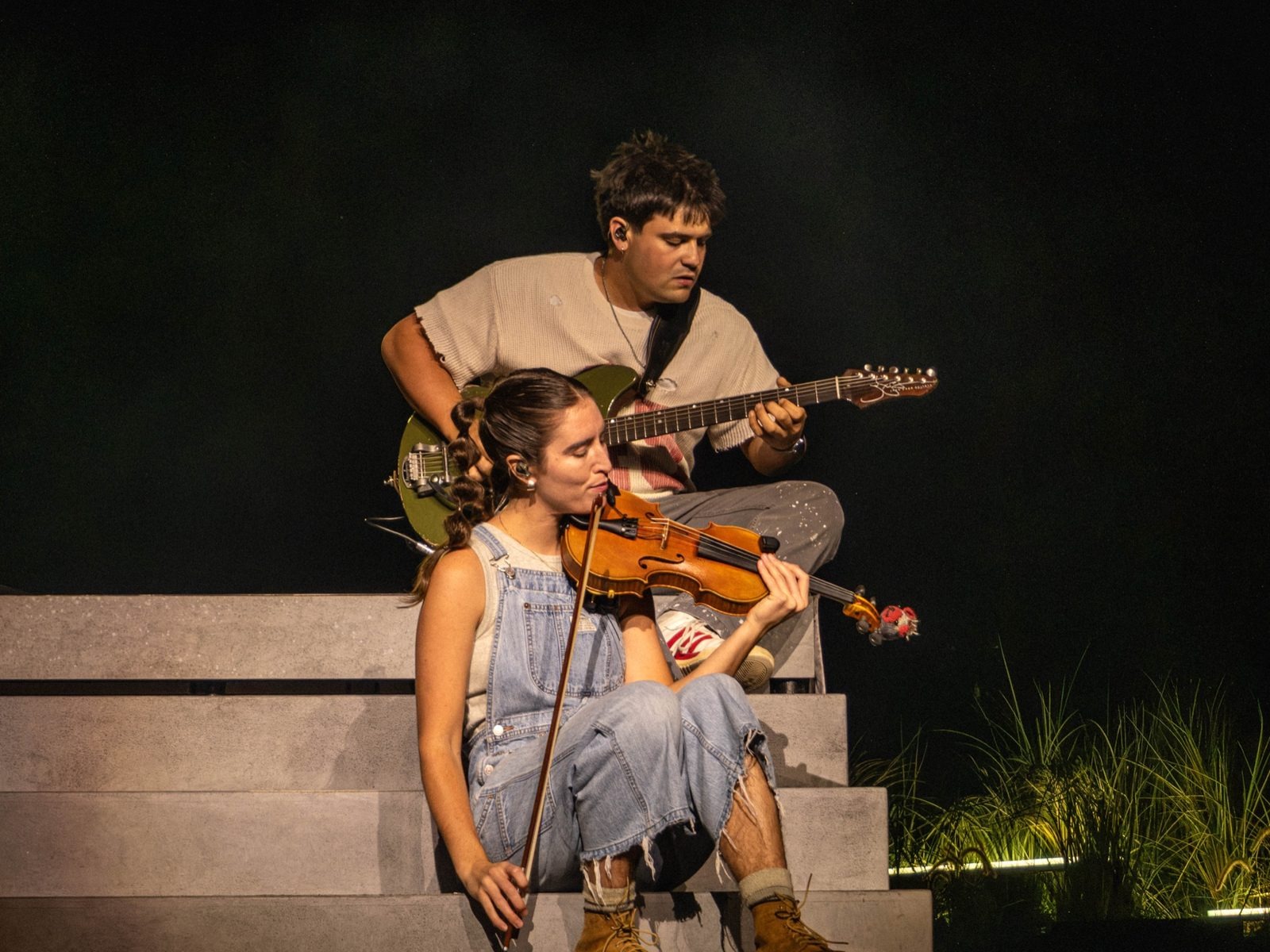 Guitarist and violinist sitting together on stage steps